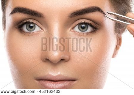 Close-up Of Female Face And Eyebrow With Tweezers