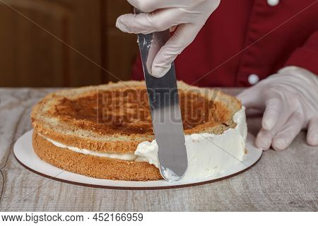 Confectioner In Burgundy Kittel Decorates Cake With Cream