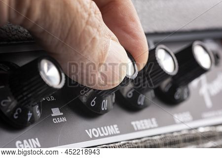 Hand Turning Up The Volume Of A Guitar Amplifier, Treble And Bass Control Knobs Out Of Focus , Equal