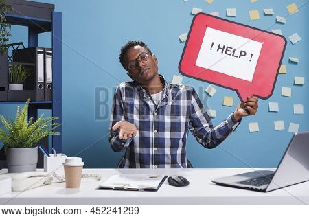 Confused And Clueless Company Office Worker Holding Help Cardboard Bubble Sign While Shrugging In Wo