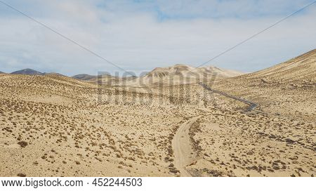 Path Road In The Middle Of A Mountains Sand Desert With Blue Bright Sky In Background. Concept Of De