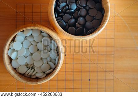 A Set Of Go Or Igo Game Stones In The Wooden Bowls On The Grid Table.