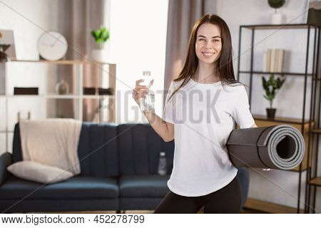 Woman Drinking Water At The Home. Muscular Woman Taking Break After Exercise. Smiling Attractive Fit