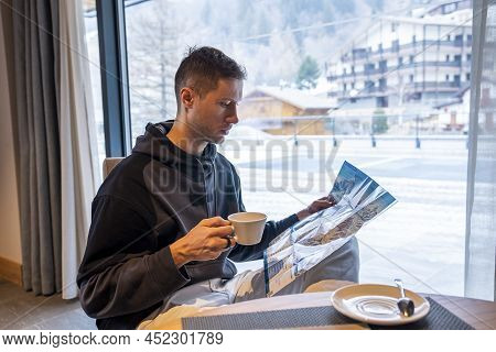 Male Tourist Analyzing Ski Map While Drinking Coffee At Resort Cafe