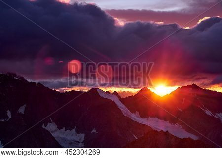 Sunset In Mountains. Reflection Of Red Sun On Mountain Snow Peaks And Clouds. Altai, Belukha Area