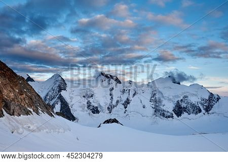 Sunset In Mountains. Reflection Of Red Sun On Mountain Snow Peaks And Clouds. Altai, Belukha Area
