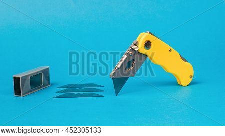 Folding Knife And A Set Of Metal Blades On A Blue Background. Reliable Hand Tool For Cutting.
