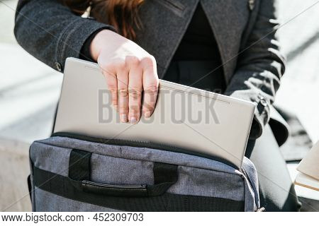 Crop Anonymous Female Freelancer In Outerwear Sitting On Concrete Bench And Taking Netbook From Case
