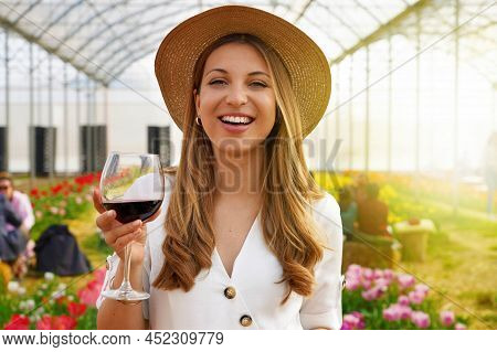 Woman Looking At Camera And Holding Glass Of Wine With People Among Flowers Field Drinking And Chatt