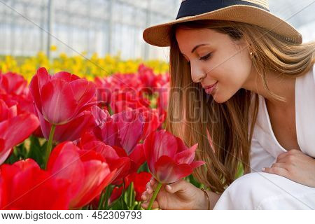 Happy Woman With Straw Hat Smelling Tulips On Farm