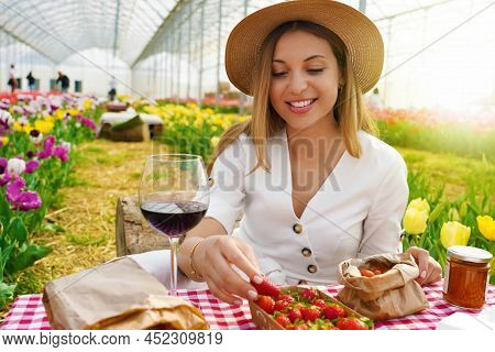Picnic Between Tulips In Spring Time. Beautiful Woman Sitting Between Flowers Enjoying Organic Local