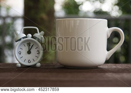 Alarm Clock Pointing At 1 O'clock With Coffee Cup On A Bench. Copy Space