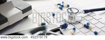 Close-up Of Medical Worker Desk, Mess On Working Place, Stethoscope Tool, Scattered Pills On Keyboar