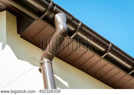 Brown Pvc Gutter Connected To Downpipe On Roof Edge And Sky.