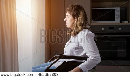 Young Disabled Woman With Cerebral Palsy Moves In Wheelchair Closer To Window Behind White Curtain A