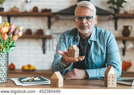 A Mature Man Holds A Miniature House In His Hands. Loss Of Money On Unprofitable Property Purchases.