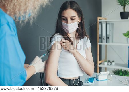 Nurse Giving The Covid-19 Vaccine To A Caucasian Woman In Facial Mask Due To Pandemic. Accination Co