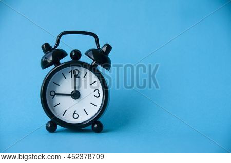Black Alarm Clock Isolated On Light Blue Background. The Clock Set At 9 O'clock. Copy Space.