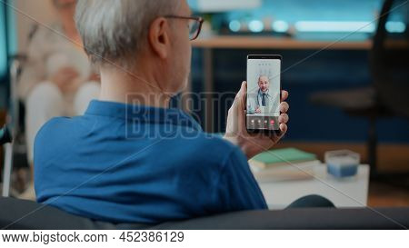 Elderly Person Calling Doctor On Videoconference To Attend Consultation, Using Mobile Phone For Tele