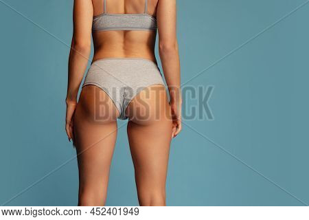 Studio Shot Of Slim, Sportive Female Body In Gray Comfortable Underwear Isolated Over Blue Backgroun