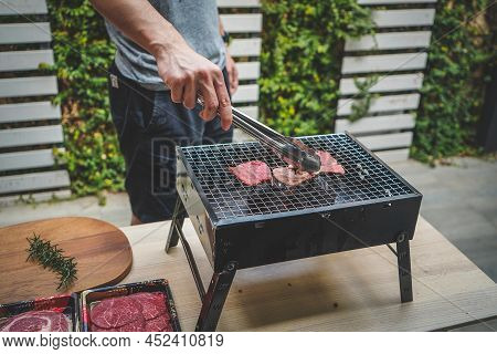 Close Up View Of Pieces Of Sliced Beef On Charcoal Grill At Outdoor Party. Human's Hands Using Meat 