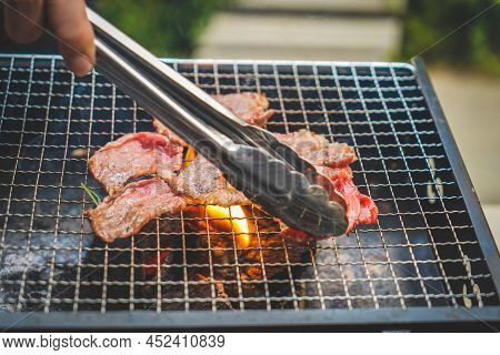 Close Up View Of Pieces Of Sliced Beef On Charcoal Grill At Outdoor Party. Human's Hands Using Meat 