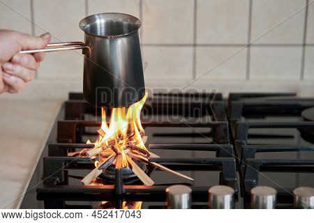 The Rise In Price Of The Gas Tariff. A Hand Holds A Jezva Over The Kitchen Stove. Instead Of Gas, A 