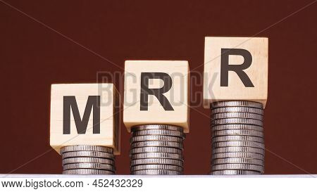Text Mrr Written On Wooden Blocks With Stacked Coins On Brown Background