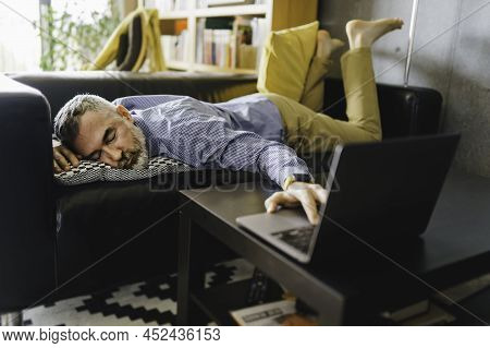 Mature Man Feeling Stress And Tired Of The Computer Lay On The Couch With A Laptop In Front