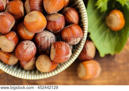 Hazelnuts Close-up In A Green Cup On A Wooden Table. Whole Nuts With Green Leaves. Harvest Of Hazeln