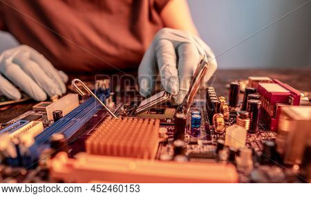 The Engineer's Gloved Hand Is Holding The Cpu Chip Against The Background Of The Motherboard. Concep