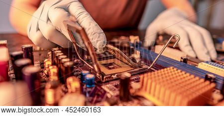 The Engineer's Gloved Hand Is Holding The Cpu Chip Against The Background Of The Motherboard. Concep
