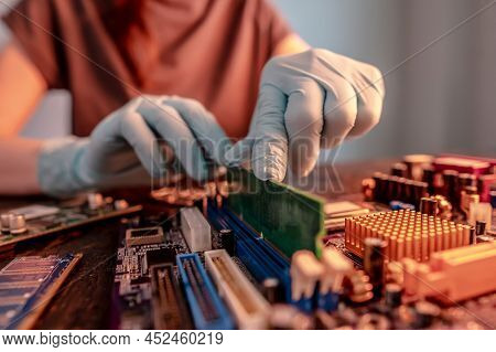 The Engineer's Gloved Hand Holds The Computer's Ram Chip Against The Background Of The Motherboard. 