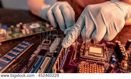 The Engineer's Gloved Hand Holds The Computer's Ram Chip Against The Background Of The Motherboard. 