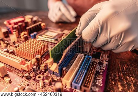 A Repair Engineer Holds A Ram Chip With His Hands In Black Gloves, Inserts The Computer's Ram Into T