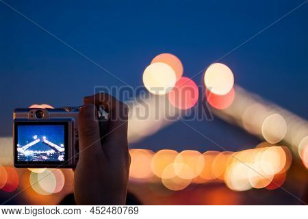 Hand With A Silver Compact Camera Shooting Night Scene, Selective Focus On A Camera With Lens Blur O