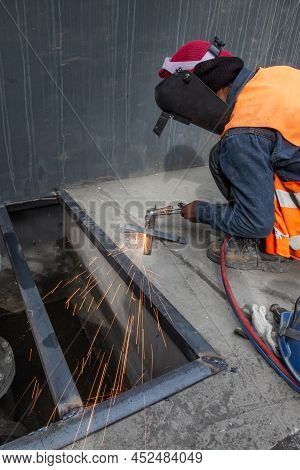 An Asian Man Welding A Metal Grate, Arc Welding Process With Sparks. Long Exposure. Focus On Sparkli