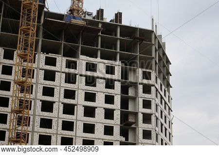 Construction Yellow Crane Builds A Tall Multi-apartment Residential Building From White Bricks And C