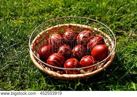 Defocus Closeup Of Basket Of Colored Red Eggs On Nature Green Grass Background. Easter Holiday Conce