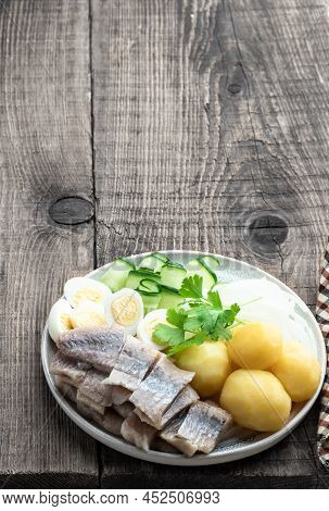 Salted  Herring With Boiled Potatoes And Quial Eggs On A White Plate On Wooden Table