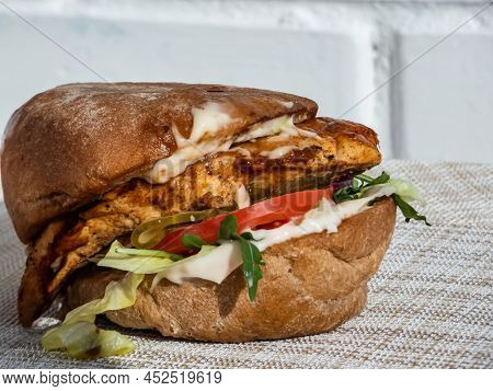 Close-up Shot Of Juicy Chicken Burger With Grilled Chicken Fillet, Ciabata, Burger Sauce, Arugula, P