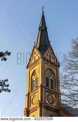 Vertical View To Yellow Stone Church Tower With Metal Roof With Green Pine Tree And Leafless Spring 