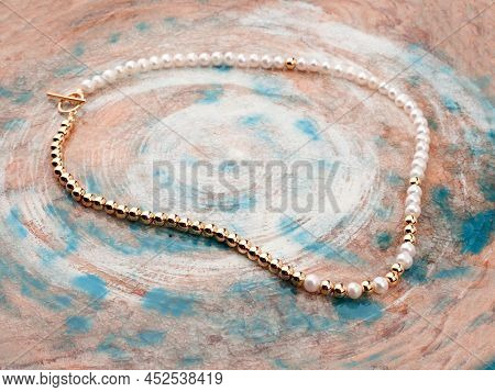 White Pearl Golden Necklace On Beige Blue Spotted Textured Background
