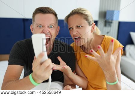 Man And Woman Scream Into Phone In Hotel Room. Dissatisfied Angry Service Customers In Hotel Concept