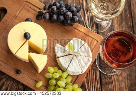 Various Types Of Cheese With Dark And Green Grapes And Wine On Wooden Table.