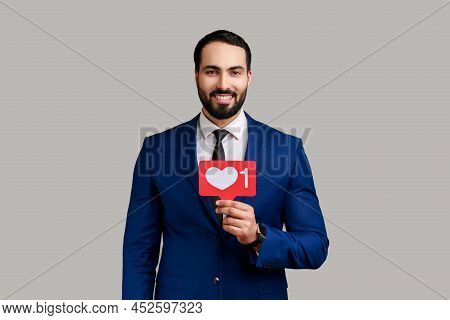 Delighted Bearded Man Holding Heart Like Icon Of Social Media, Notification Button To Follow, Subscr