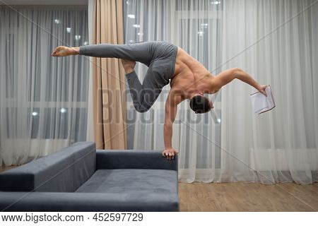 Man Keep Balance On One Hand And Reads A Book Indoor. Concept Of Willpower, Motivation And Passion
