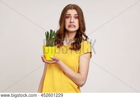Portrait Of Attractive Young Female Wearing Yellow Casual T-shirt Holding Tricky Cactus In Flower Po
