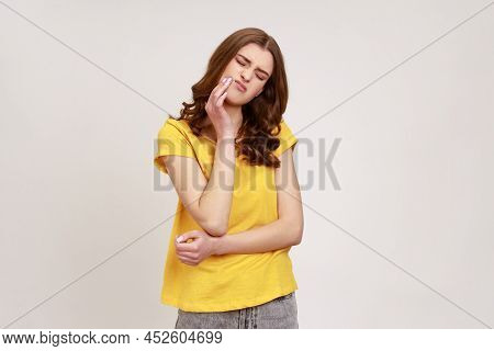Frustrated Wavy Haired Teenager Girl Wearing Yellow Casual T-shirt Touching Cheek And Wincing In Pai