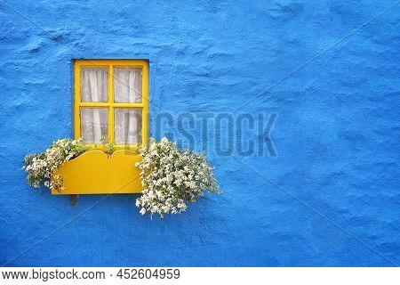 Rustic Blue Cottage Wall With Yellow Wooden Window Frame And Flower Box